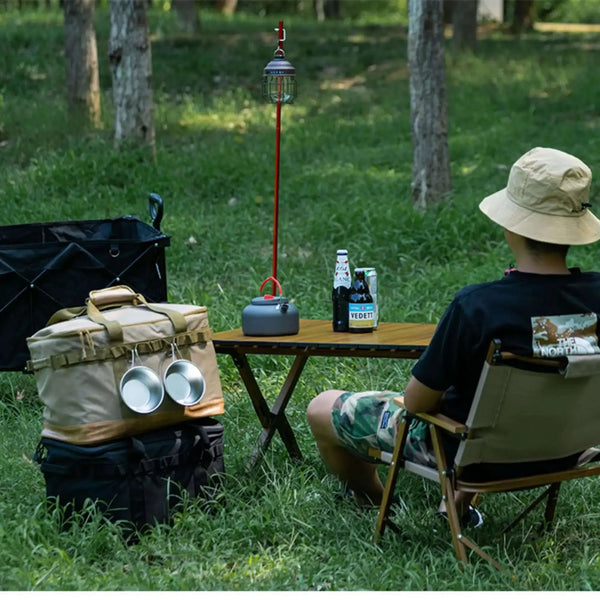 Un campeur se détend avec son équipement, y compris une boîte de rangement pliable avec un cadre en métal, parfaite pour organiser les essentiels du camping dans la nature.