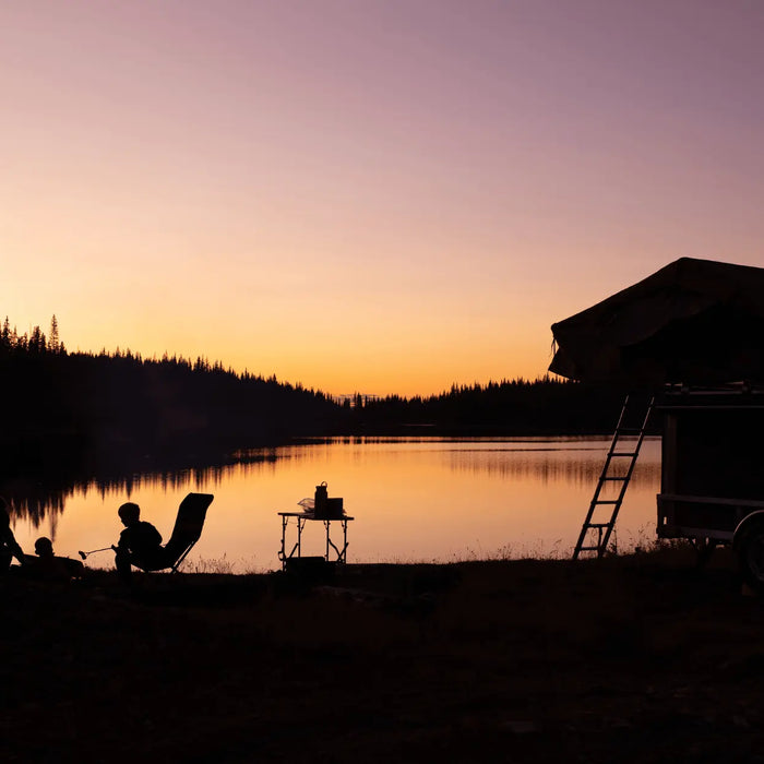 Rooftop tent setup by a lake with sunset backdrop, ideal for camping enthusiasts exploring benefits over traditional caravans and tents.