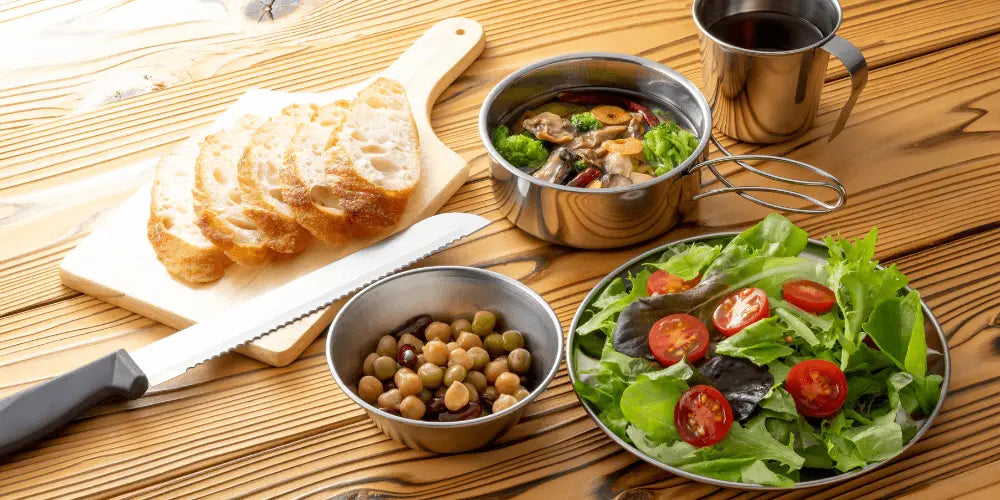 Camping meal with fresh salad, sliced bread, mixed olives, and a thermos, perfect for roof tent meals without a fridge.