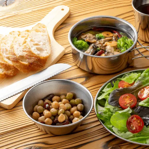 Camping meal with fresh salad, sliced bread, mixed olives, and a thermos, perfect for roof tent meals without a fridge.