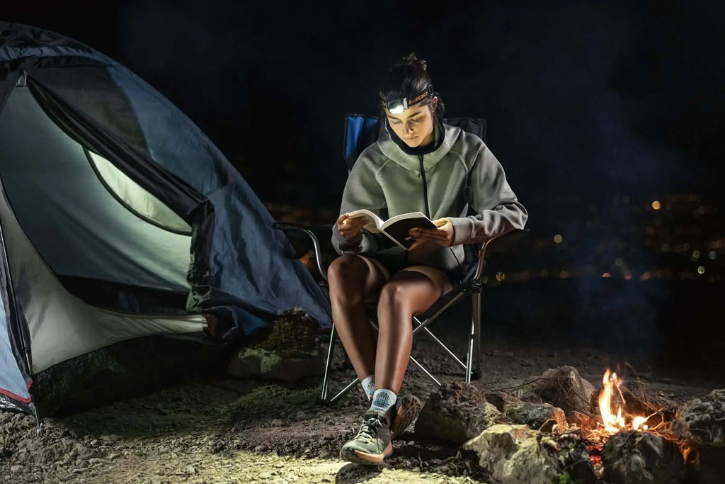 Camper reading at night with LAGOLIGHT headlamp beside tent and campfire