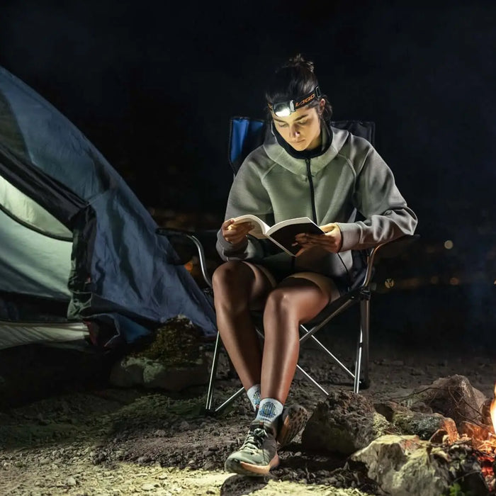 Camper reading at night with LAGOLIGHT headlamp beside tent and campfire