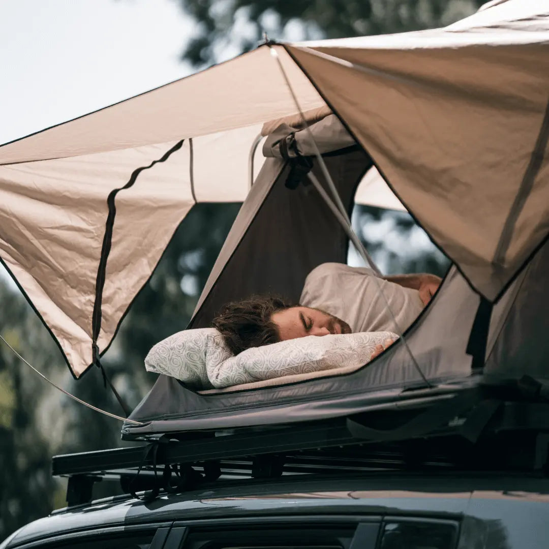 Person sleeping comfortably on a rooftop tent with ergonomic pillow, showcasing ideal camping sleeping accessories.