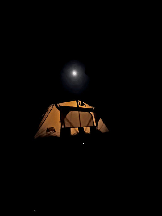 Une tente de camping illuminée la nuit sous une pleine lune, mettant en valeur l'ambiance d'aventure en plein air.