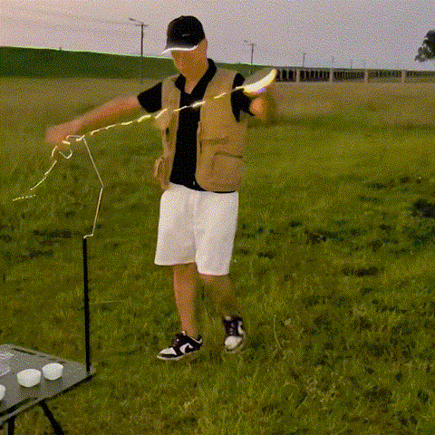 Person setting up a portable retractable string light on a grassy field for outdoor camping ambiance.