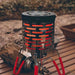 Mini chauffage réchaud à gaz en acier portable pour camping, sur une table en bois, entouré de nature, idéal pour l'extérieur.