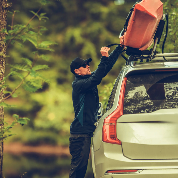 Un homme fixe une tente de toit avec un écrou universel M8 sur un SUV dans un cadre forestier.
