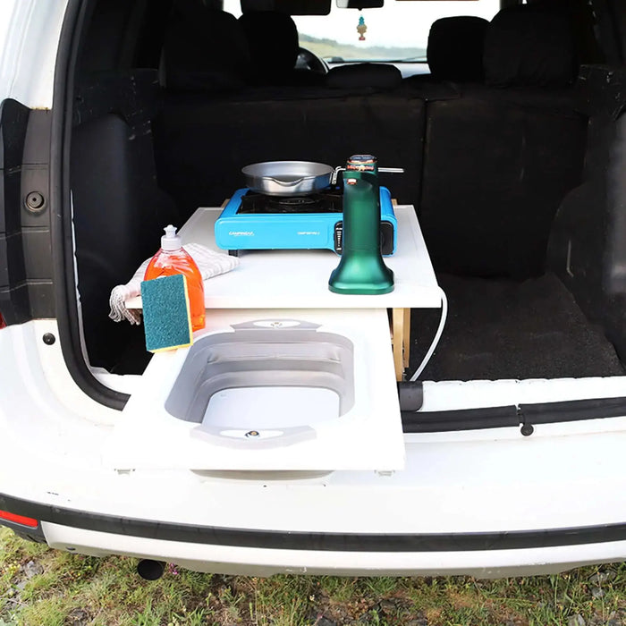 Aménagement d'une cuisine de camping dans le coffre de la voiture avec espace de rangement, évier et réchaud portable pour plus de commodité lors des excursions en camping. Idéal pour une conversion de voiture compacte.