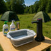 Évier pliable en silicone sur une table de camping avec des ustensiles et un réchaud à gaz, idéal pour la cuisine en plein air.