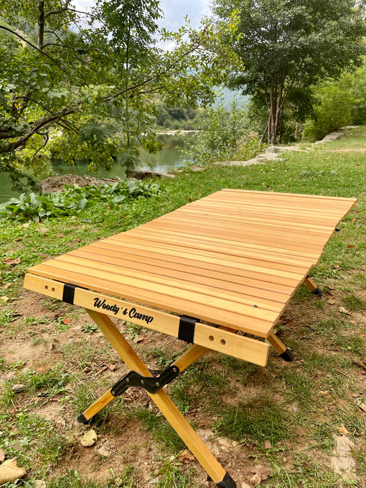 louer materiel camping table chaise montpellier location herault 34000 woodys camp Table de camping en bois pliable installée en extérieur avec des chaises, des boissons et de la nourriture, mettant en avant un design durable pour des repas confortables en plein air.
