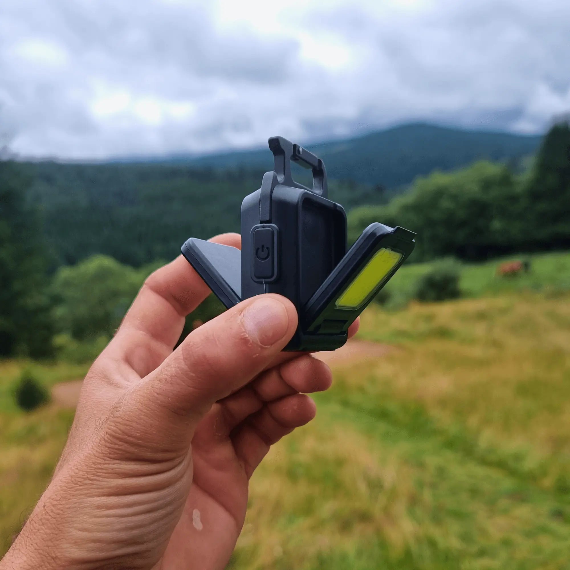 Person holding an ultrapuissant Mini LED flashlight with lush green landscape in the background.