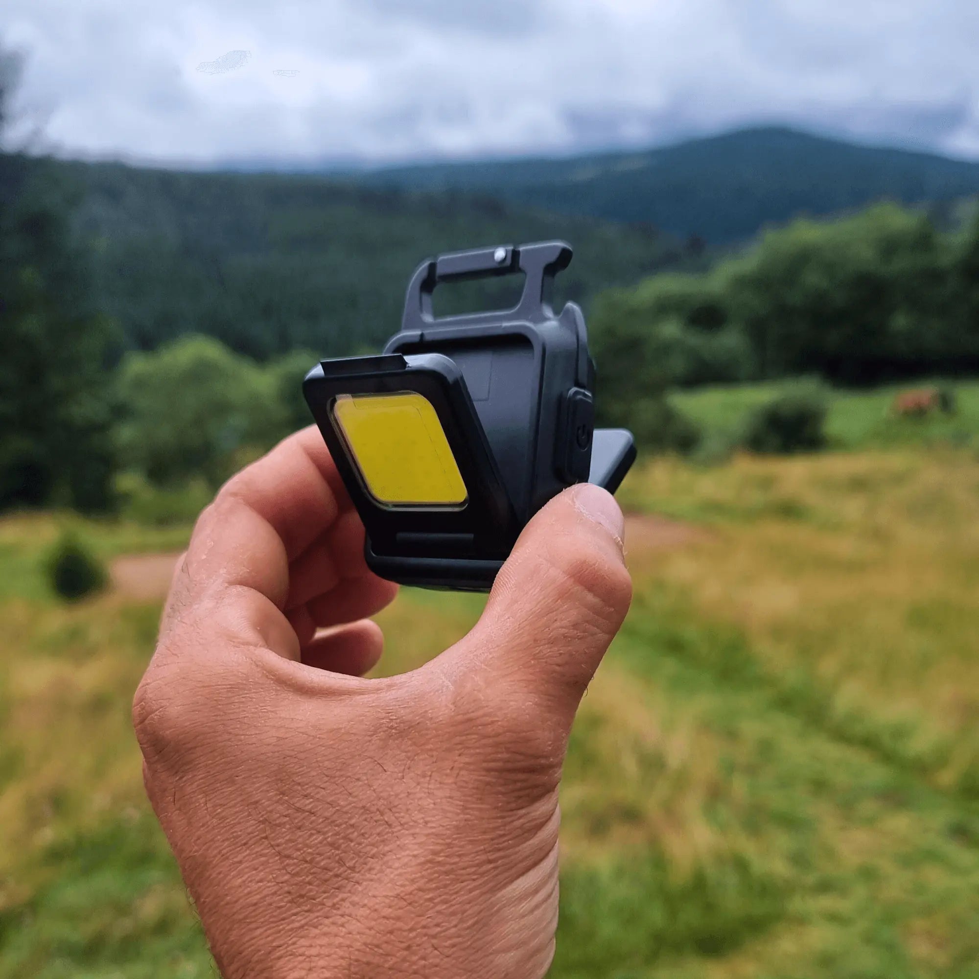 Hand holding a mini LED flashlight in a scenic outdoor setting, showcasing its compact design and ultrabright capabilities.