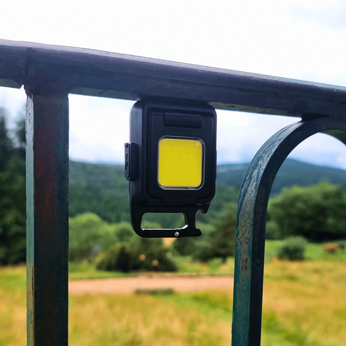 Une mini lampe de poche LED compacte suspendue à une clôture, idéale pour les aventures en plein air, affichant son faisceau lumineux ultrapuissant.