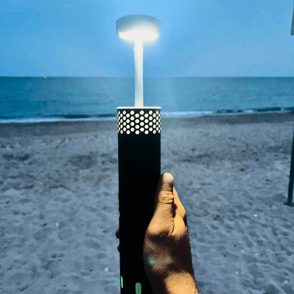 Portable rechargeable LED telescopic lamp illuminating a beach scene, perfect for camping and outdoor adventures.