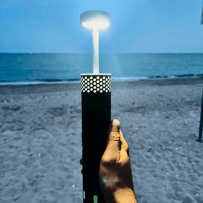 Lampe LED télescopique rechargeable et portable illuminant une scène de plage, parfaite pour le camping et les aventures en plein air.