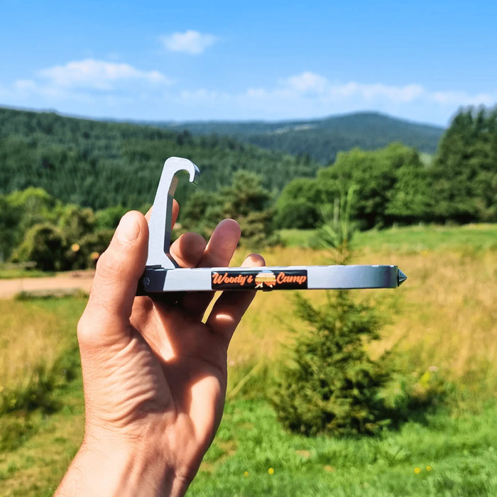 Une main tenant une étape de tente de toit dans un cadre extérieur pittoresque avec une végétation luxuriante et des montagnes en arrière-plan.