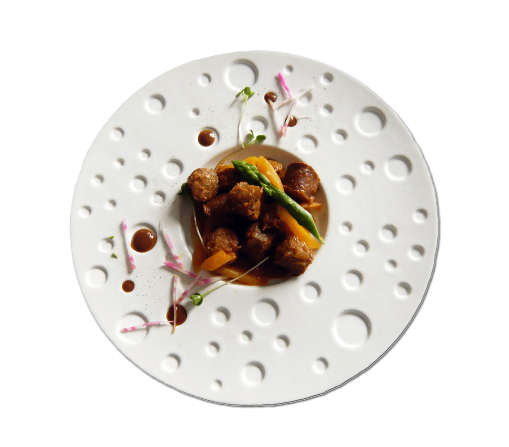 Plat gastronomique avec des boulettes de viande, des asperges et une sauce sur une présentation artistique dans une assiette blanche.