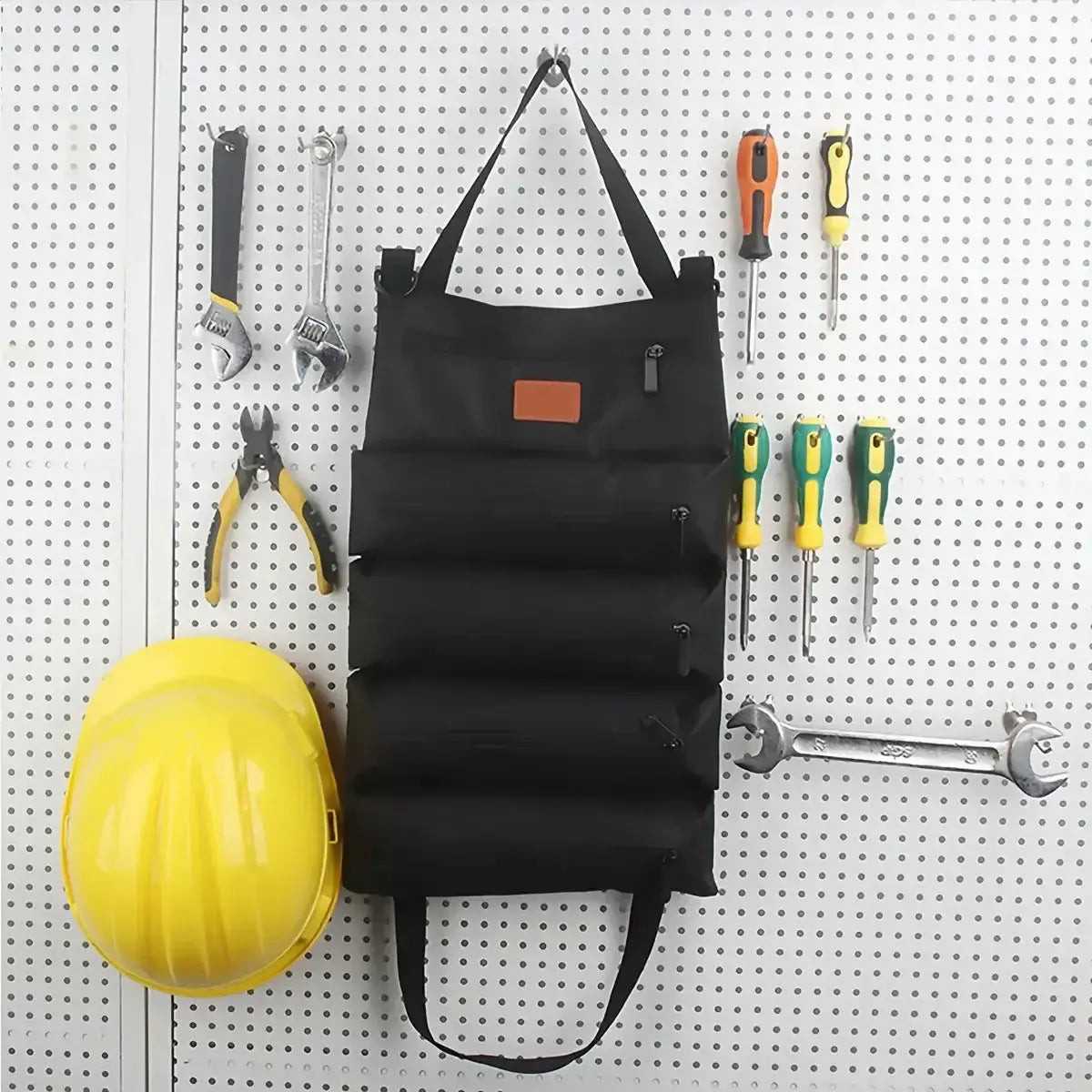 Sac de rangement pliable avec compartiments, accroché, entouré d'outils, sur un fond de panneau perforé.