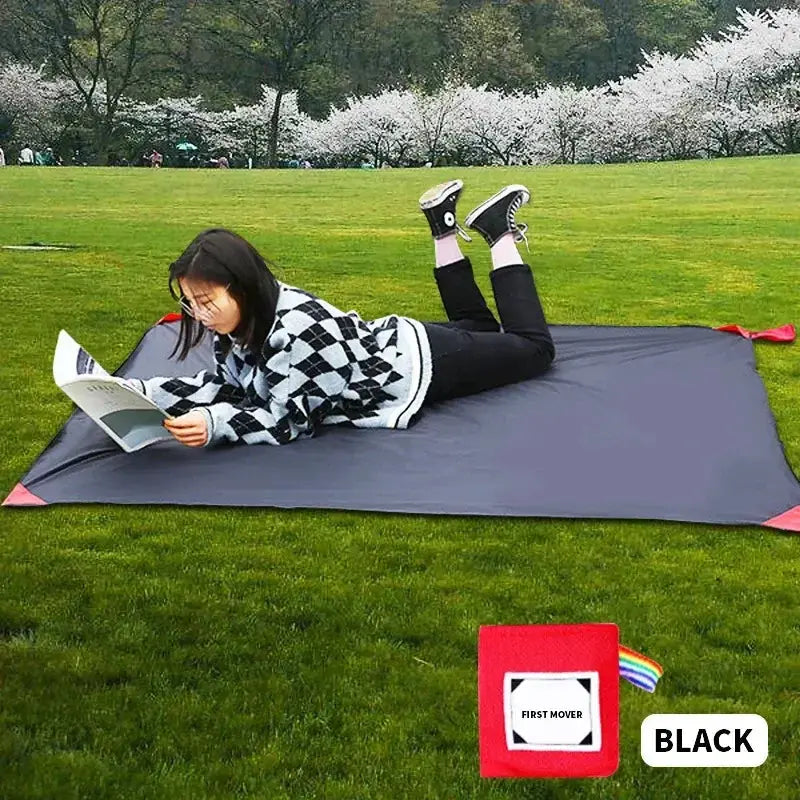 Person reading on a black outdoor pocket mat in a grassy park, showcasing comfort and portability for camping and outdoor activities.