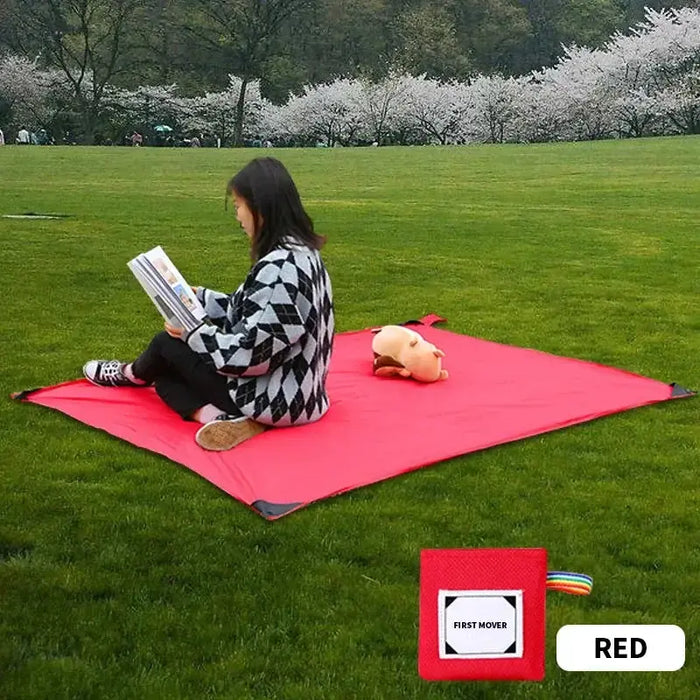 Une personne assise sur un tapis de poche rouge sur l'herbe, lisant un livre, avec un jouet en peluche à ses côtés.