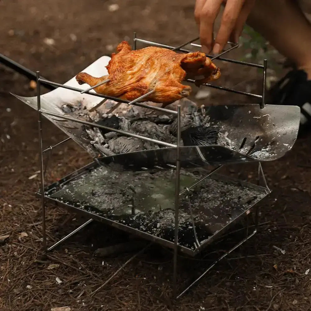 Portable stainless steel camping grill cooking chicken over open fire outdoors.