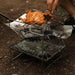 Gril de camping en acier inoxydable portable cuisinant du poulet sur un feu de bois en plein air.