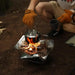 Cuisine en plein air avec un grille-pain en acier inoxydable pliant, mettant en valeur son design compact et sa construction robuste pour les aventures de camping.