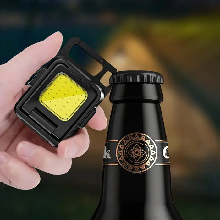 Main tenant une petite lampe de poche LED près d'une bouteille, mettant en valeur son design portable et sa capacité lumineuse puissante.