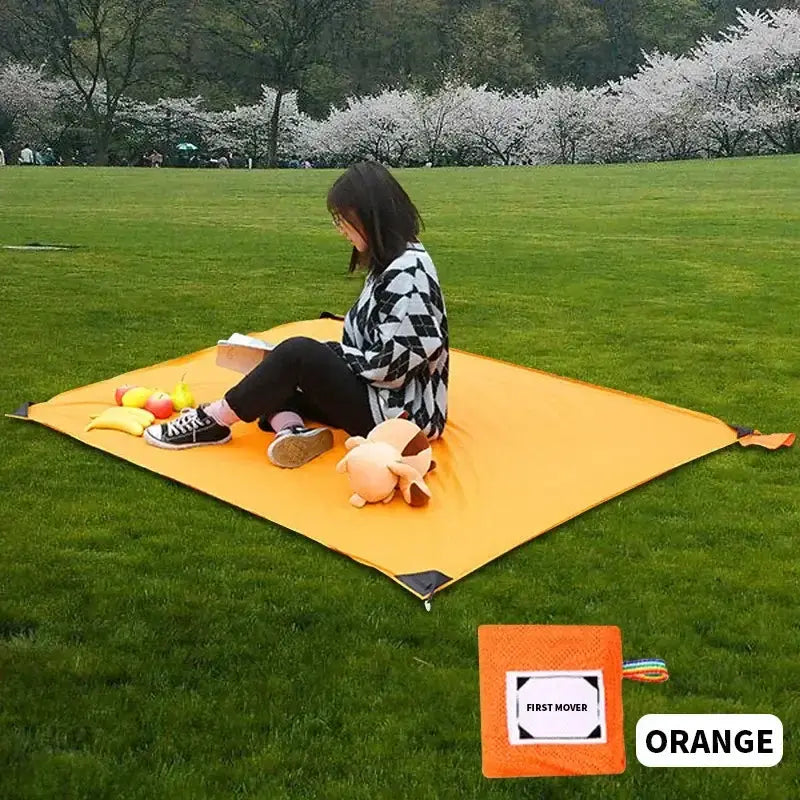Woman sitting on an orange portable camping mat in a park, ideal for picnics, beach outings, nature relaxation, festivals, or hiking.