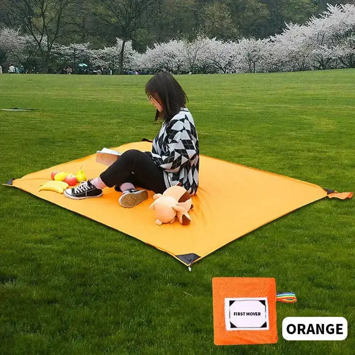 Femme assise sur un mat de camping portable orange dans un parc, idéal pour des pique-niques, des sorties à la plage, des moments de détente dans la nature, des festivals ou des randonnées.