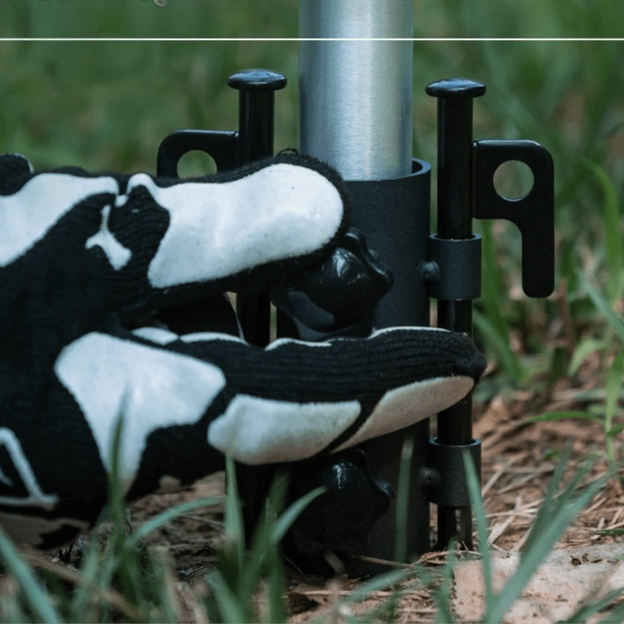 Person adjusting adjustable tent support pole in grassy area with gloved hand for outdoor camping setup.