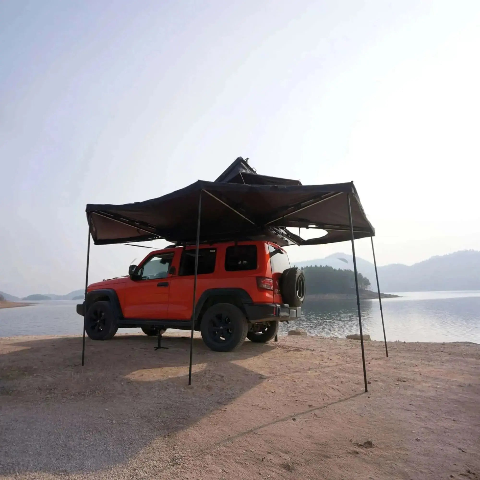 Red 4x4 with Auvent Autoportant 360° awning deployed by a lake, showcasing camping setup with integrated LEDs and aluminum arms.