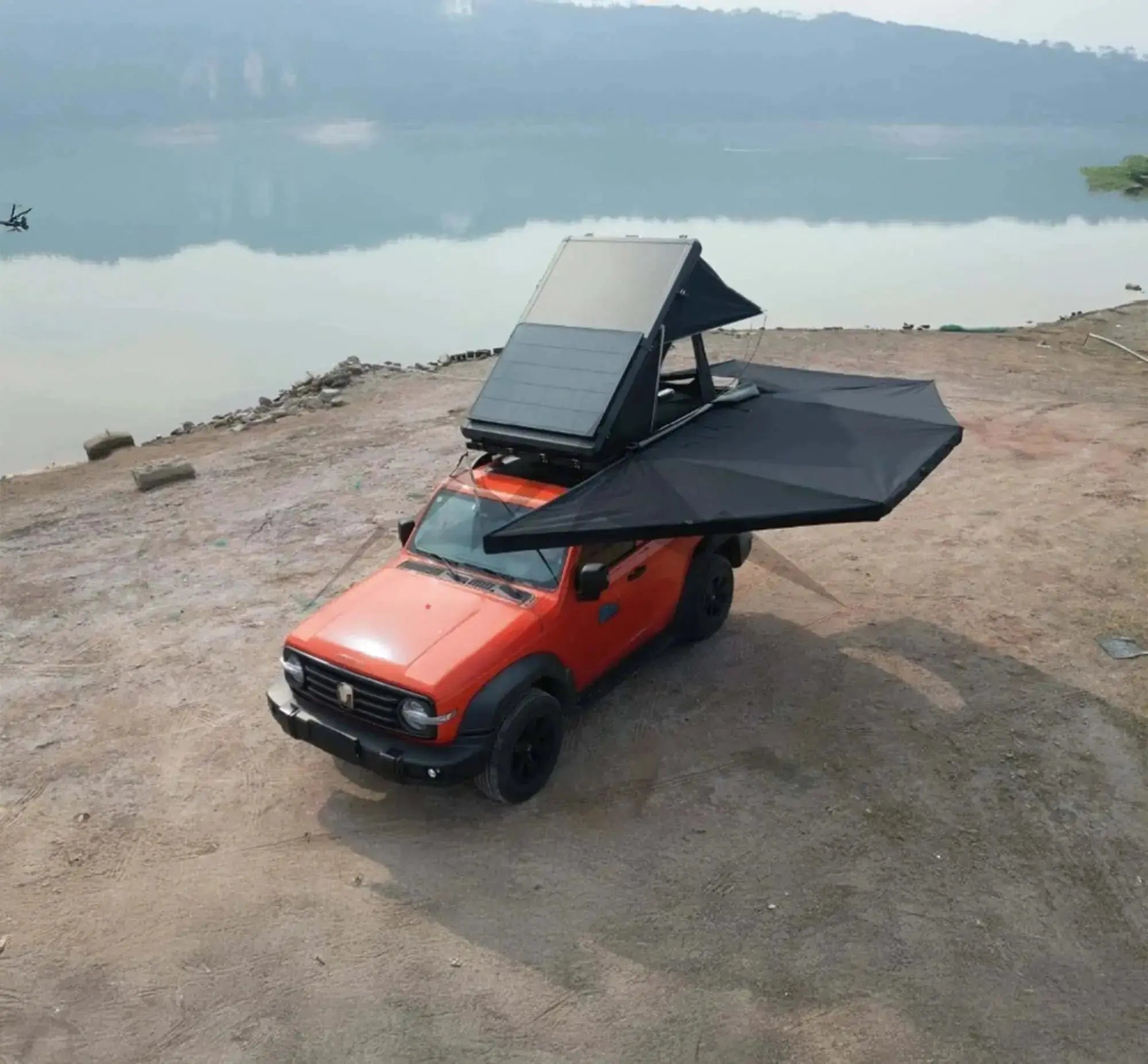 Red 4x4 with black 360° self-supporting awning and integrated LEDs, ideal for camping, parked near a lake.