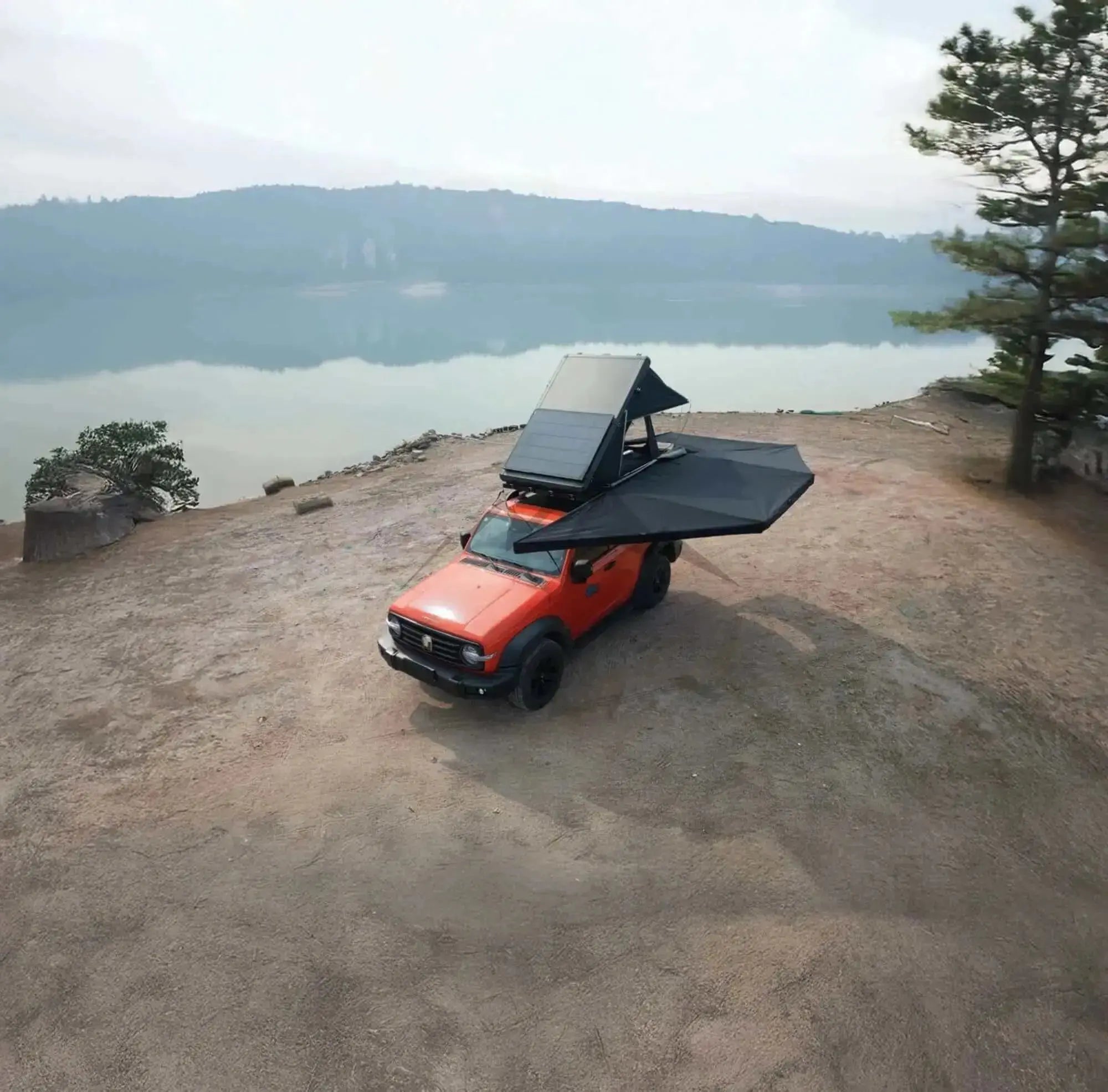 Orange 4x4 vehicle with 360° freestanding black awning and integrated LEDs, parked by a scenic lake, showcasing camping setup.
