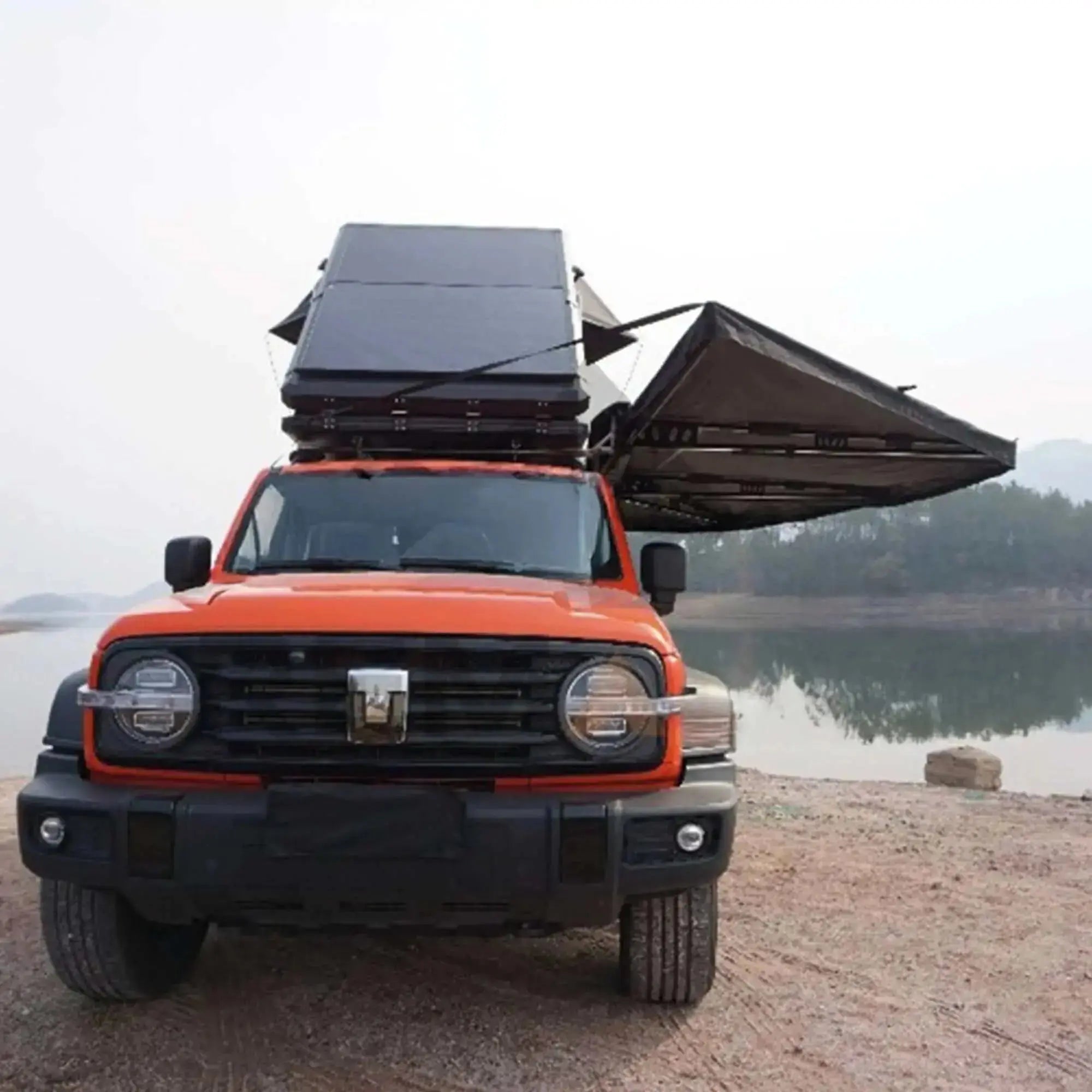 4x4 vehicle with 360° black freestanding awning with integrated LEDs, deployed near a scenic lake and mountainous backdrop.