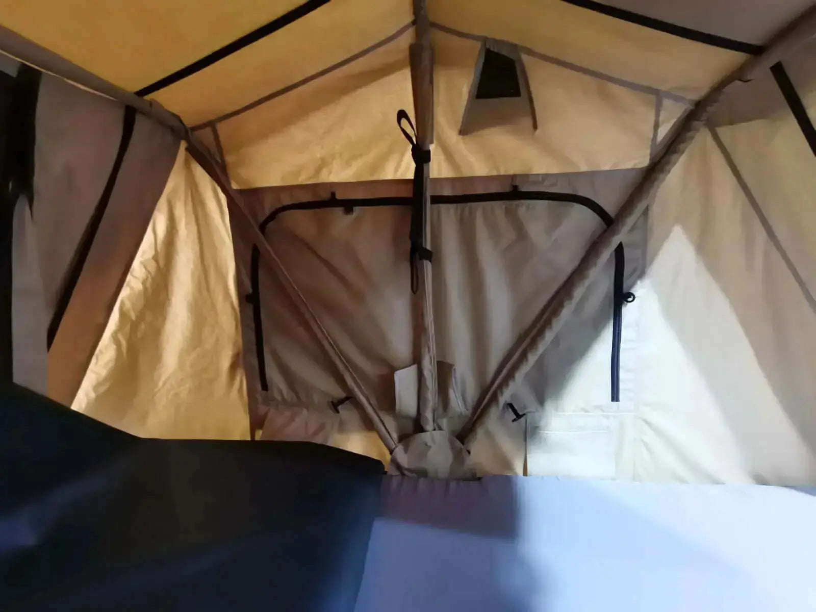 Intérieur d'une tente spacieuse avec un tissu beige et une structure solide, idéale pour les aventures en plein air et les voyages en voiture, pouvant accueillir 2 à 3 personnes.