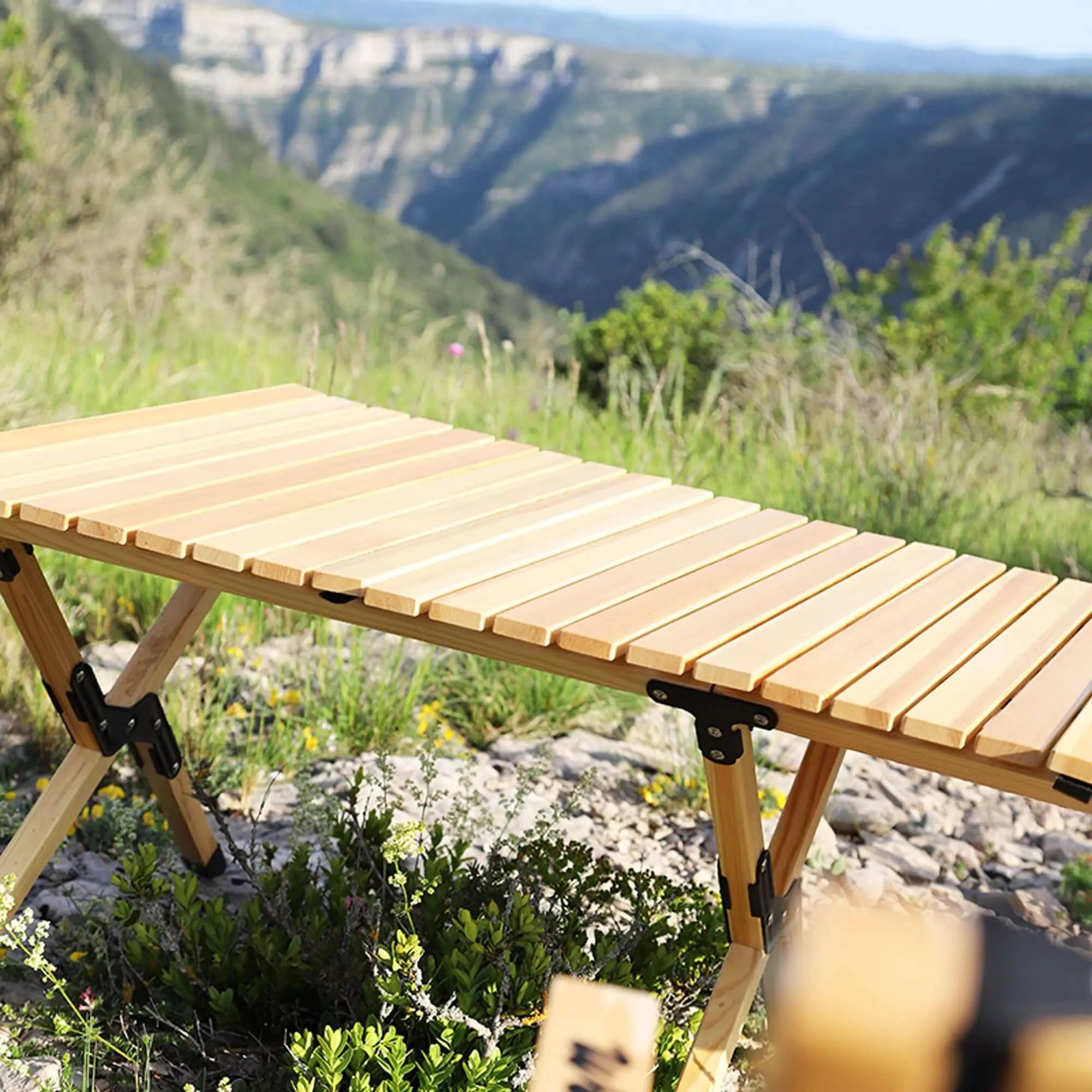 Table pliante en bois pour camping installée dans un décor montagneux, montrant sa robustesse et simplicité de rangement.