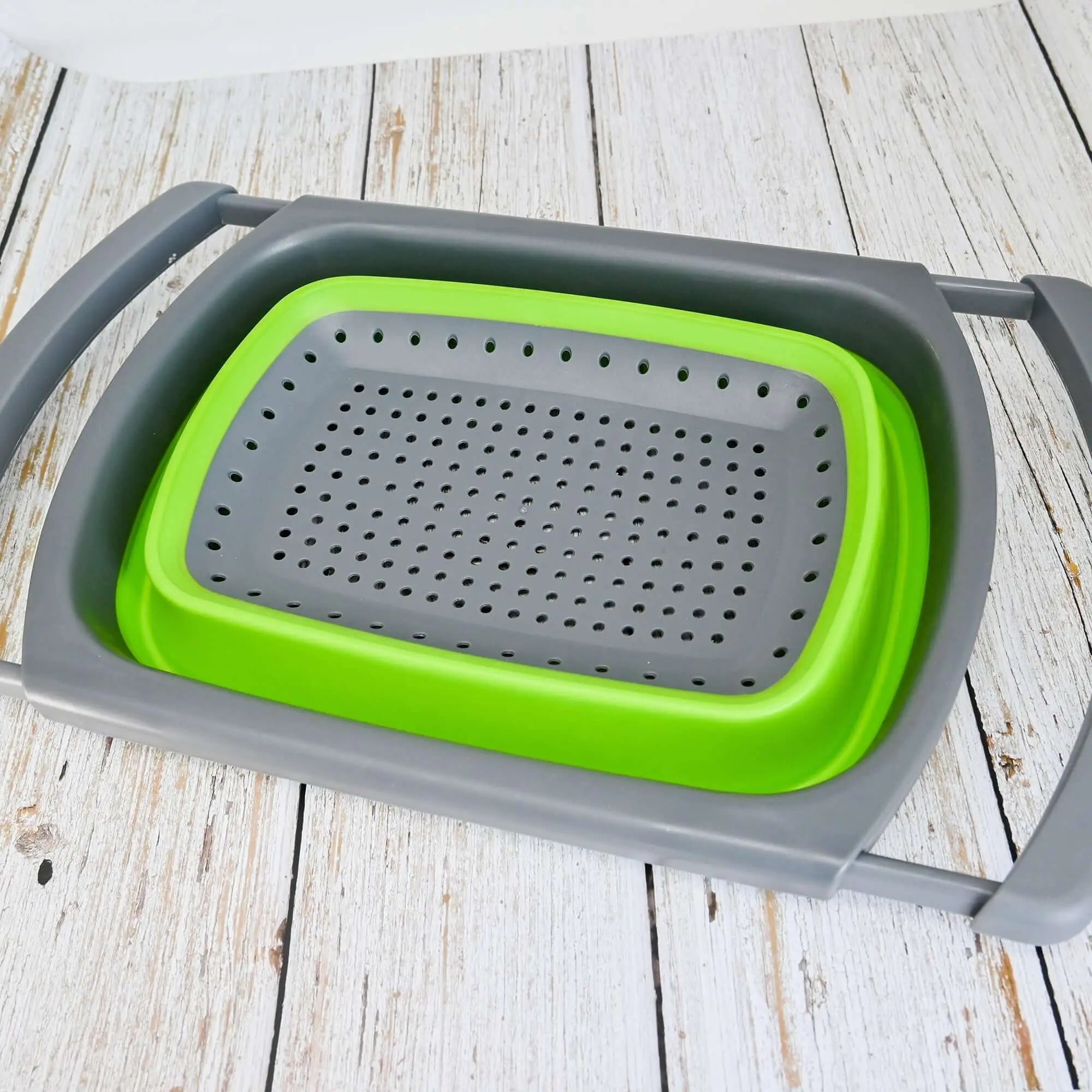 Passoire pliable en silicone verte avec poignées réglables, idéale pour le camping et les voyages, posée sur une table en bois.