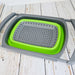 Passoire pliable en silicone verte avec poignées réglables, idéale pour le camping et les voyages, posée sur une table en bois.