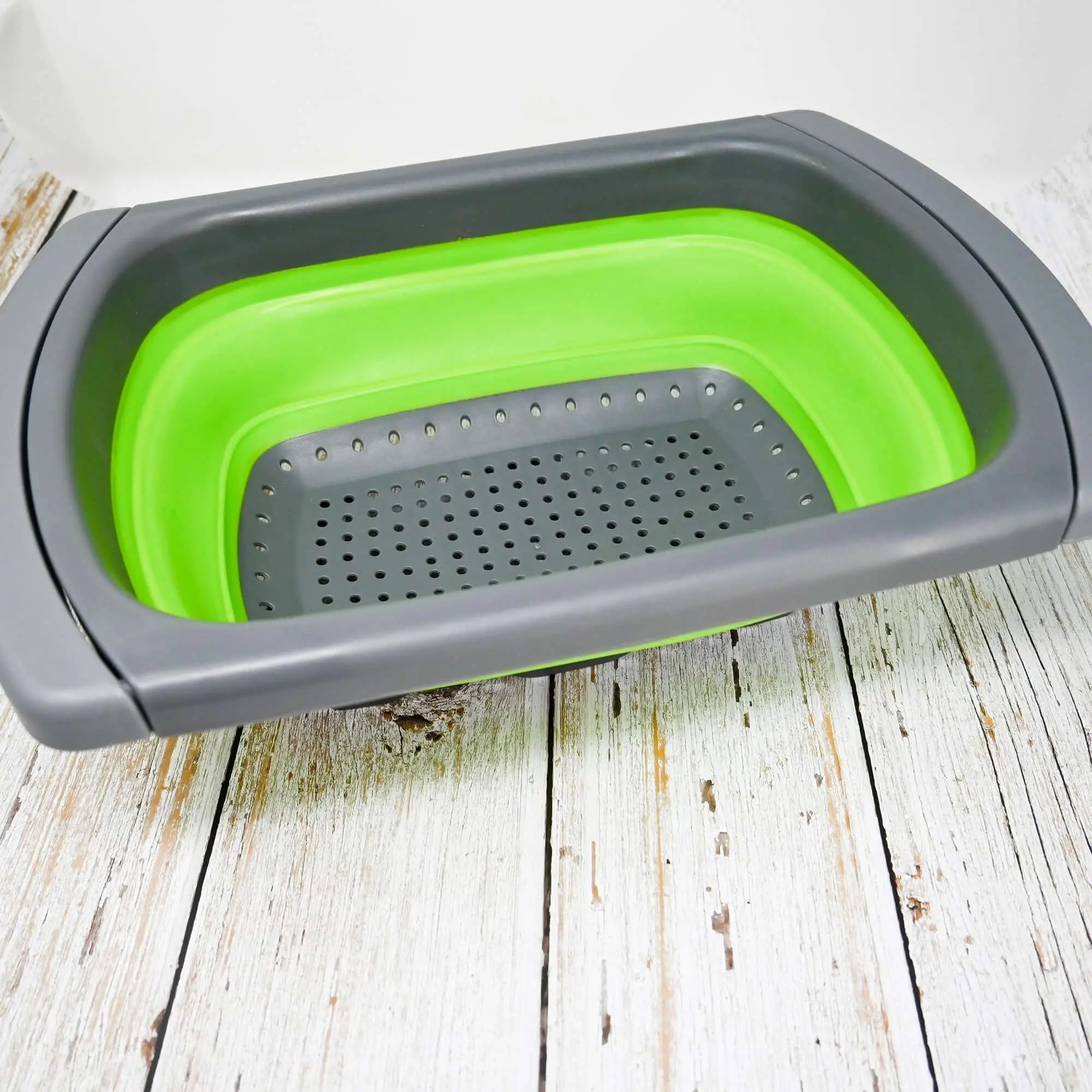Tag alt : Passoire pliable en silicone vert avec poignées réglables sur une planche en bois, idéale pour le camping et les activités en plein air.
