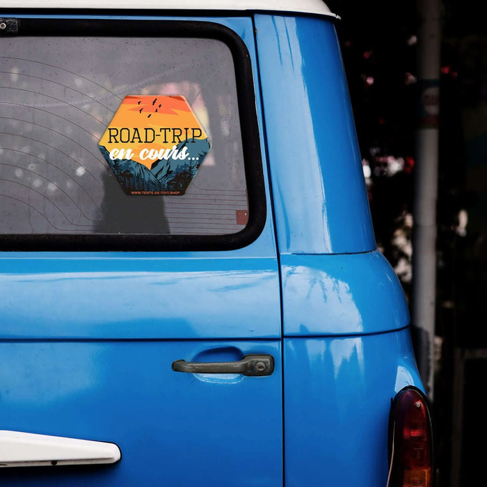 Fourgon bleu avec un autocollant coloré "Road-trip en cours", mettant en avant la passion pour le camping et les voyages en voiture. Durable et résistant aux intempéries.