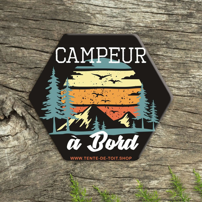 Autocollant "Campeur à bord" hexagonal avec un design coloré de montagnes et de forêt sur fond de bois, idéal pour les fans de vanlife.