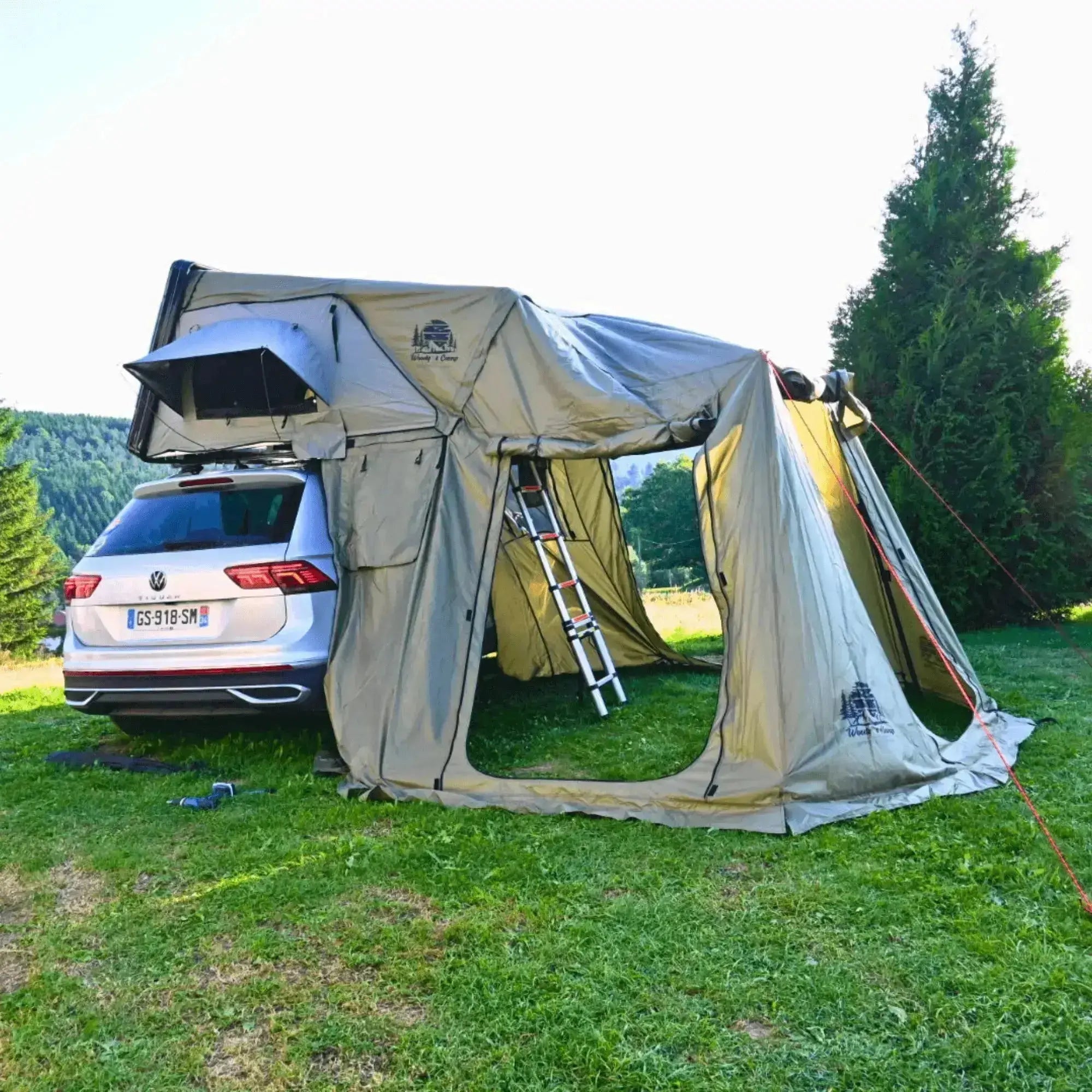 Hard shell roof tent annex with multiple openings attached to a car, providing additional living space for camping.