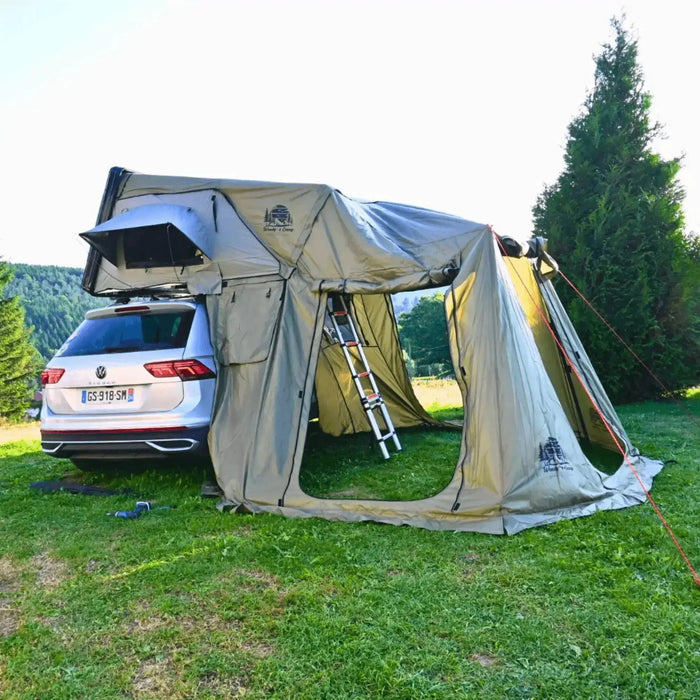Annexe de tente de toit rigide avec plusieurs ouvertures, attachée à une voiture, offrant un espace de vie supplémentaire pour le camping.