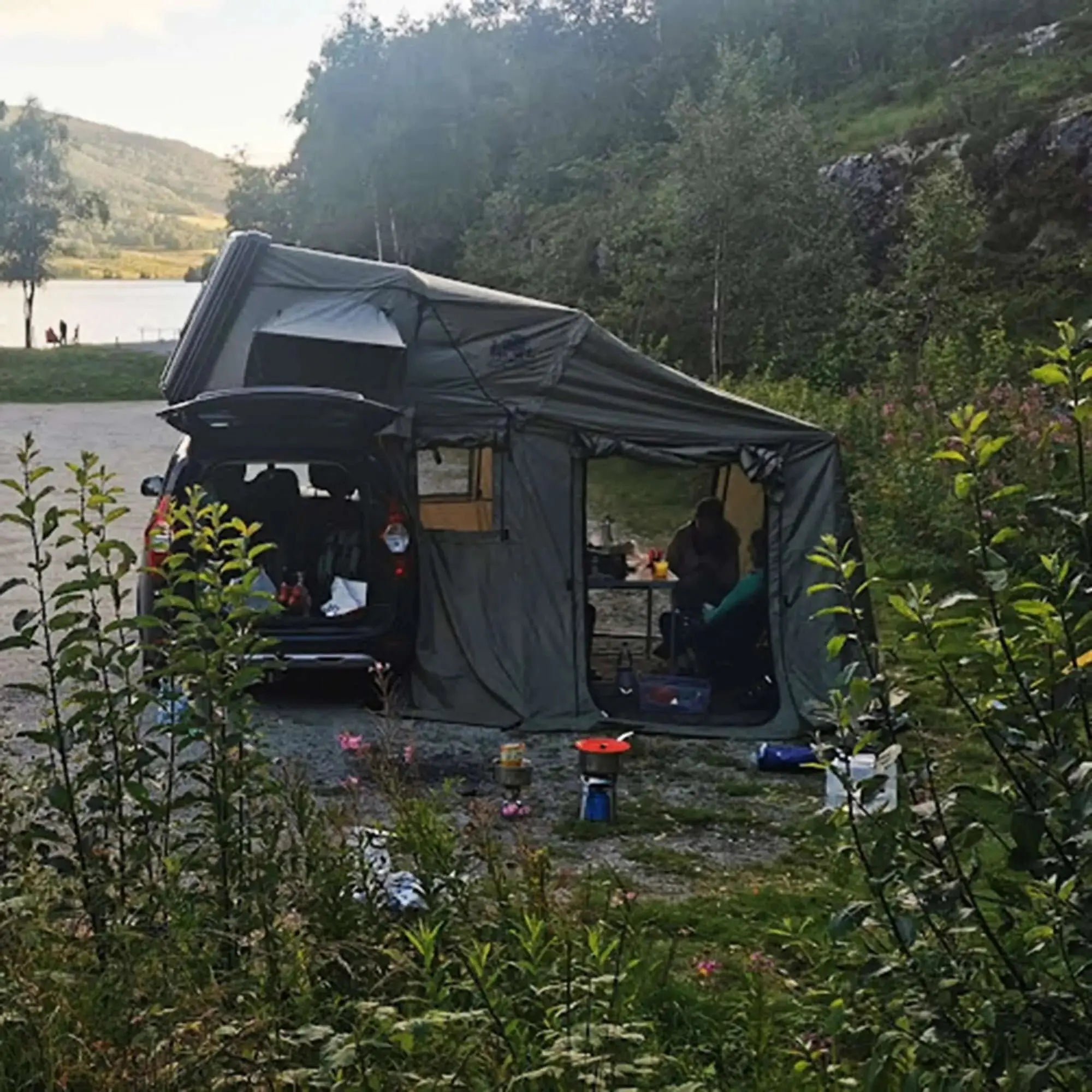 Tente de toit rigide 3 places avec annexe pour camping, installée dans un cadre naturel verdoyant au bord d'un lac.