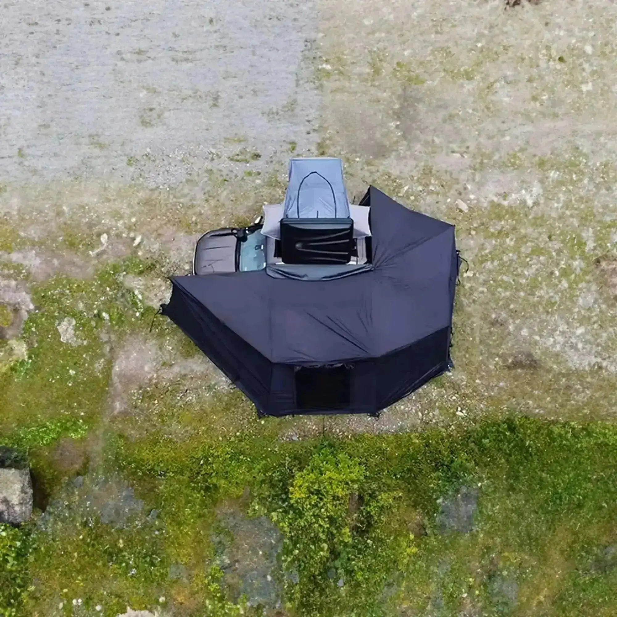 Overhead view of a self-supporting 360-degree black awning with integrated LEDs, attached to a vehicle, displayed outdoors.