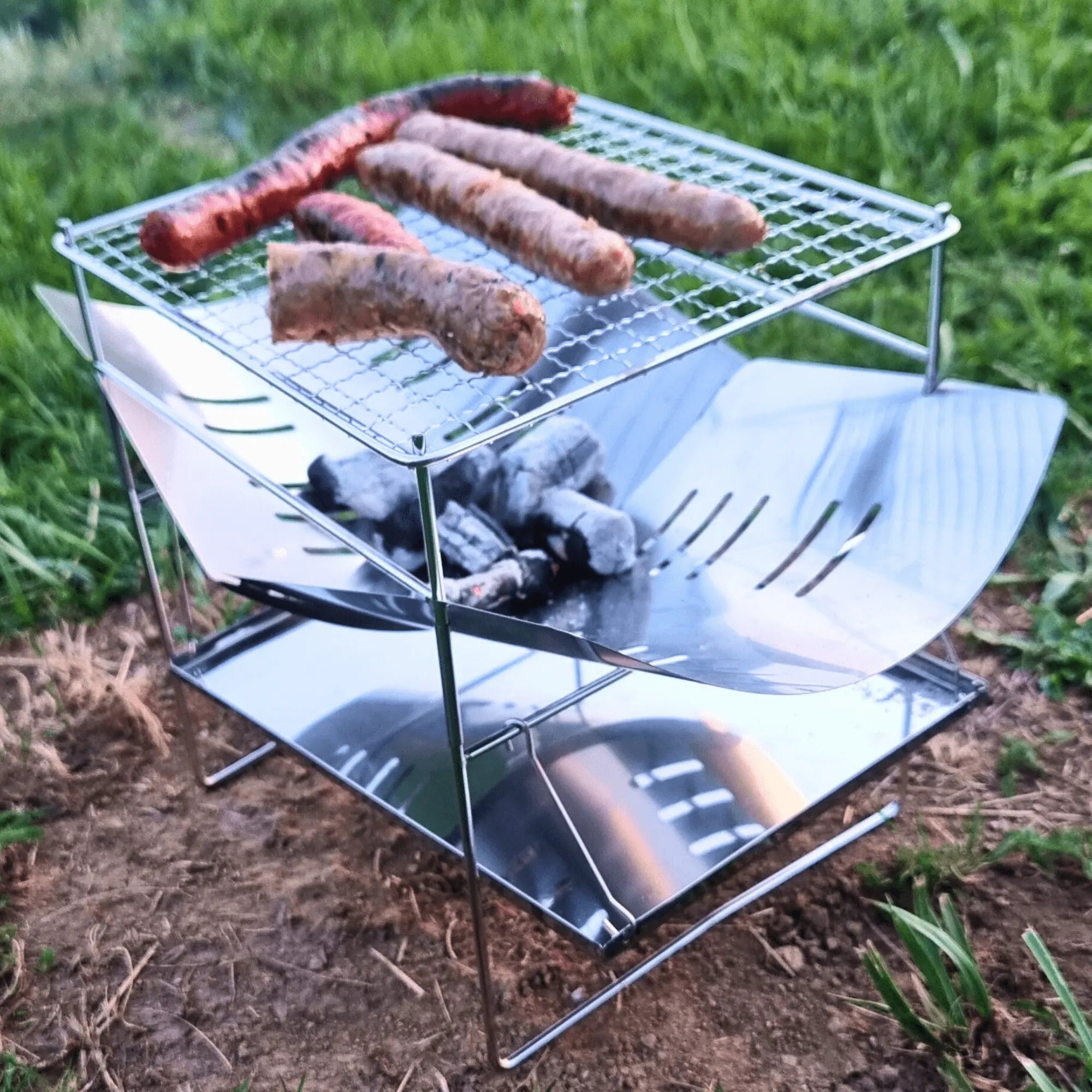 Portable stainless steel camping grill with sausages, foldable for easy transport and storage, perfect for outdoor cooking.