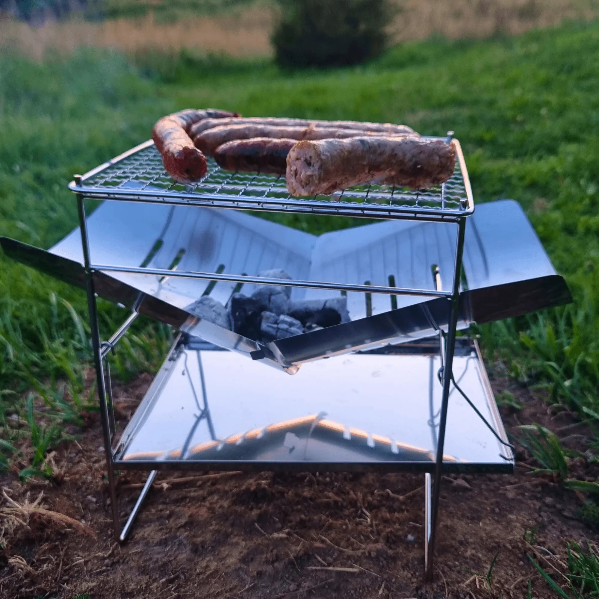 Pliant camping grill in use with sausages cooking, stainless steel design for durability, ideal for outdoor adventures.