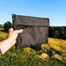 Une personne tenant un sac de grill de camping pliable noir et compact contre un arrière-plan extérieur pittoresque, idéal pour un transport et un stockage faciles.