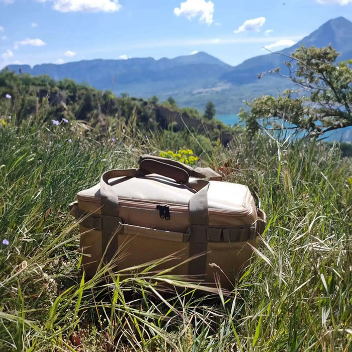 Boîte de transport pliable avec armature métallique pour le camping en plein air, posée dans un champ pittoresque avec vue sur les montagnes.